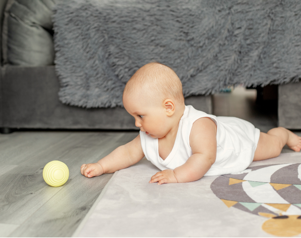 Baby ligt op zijn buik en grijpt naar een bal